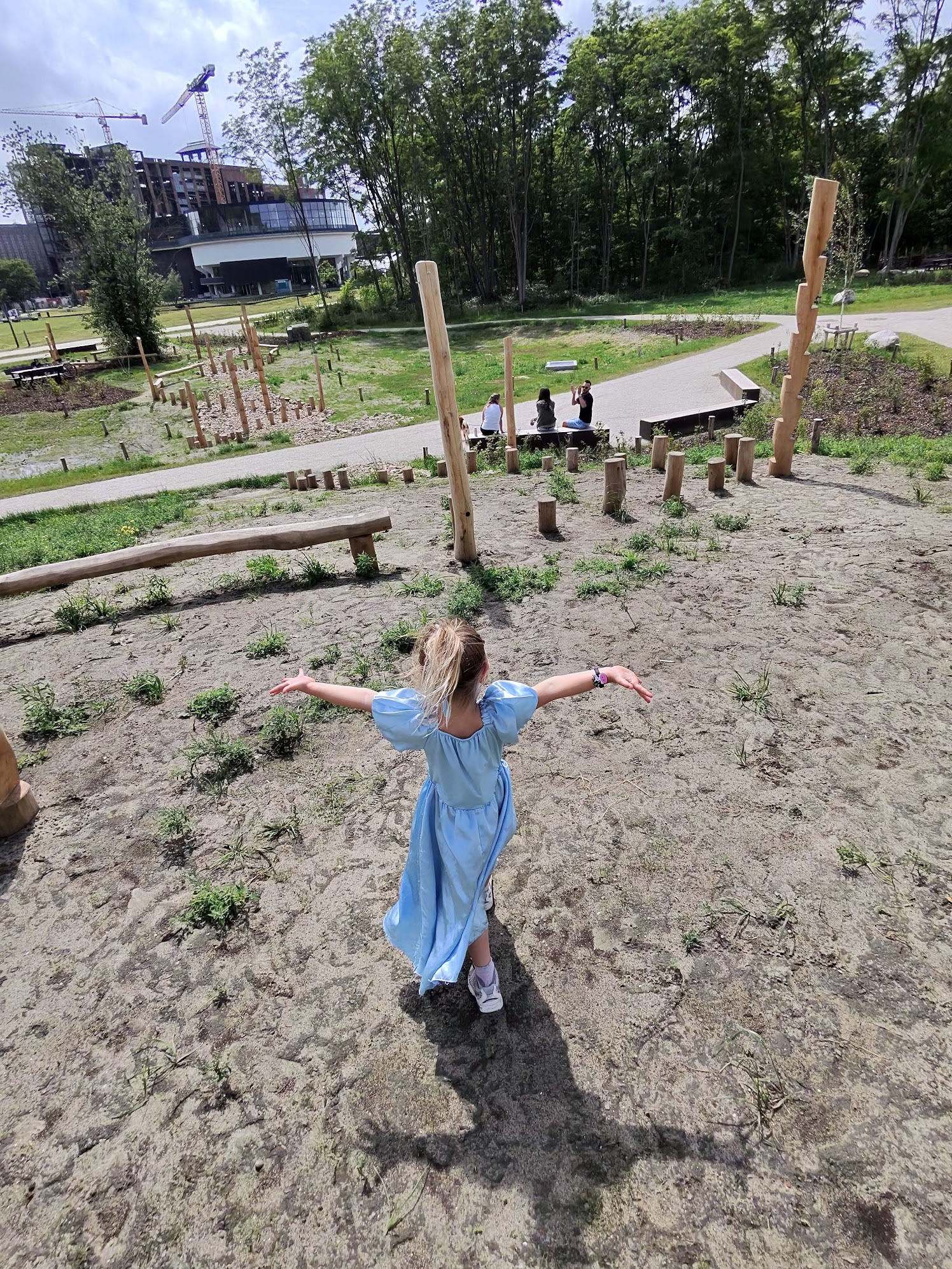 Young girl in a blue dress with arms spread wide in a park, shot from the glasses' elevated first-person perspective